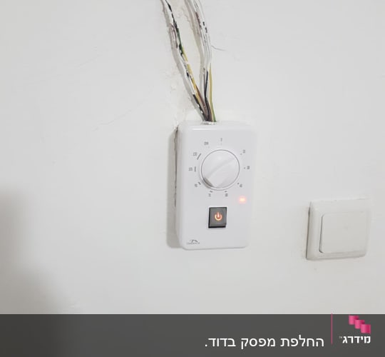 חוטי חשמל חשופים ליד תרמוסטט על קיר לבן